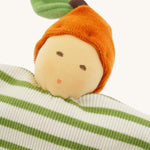 Close-up of the Nanchen Orange Baby Comforter, a handmade doll with a soft, peach-colored face, embroidered features, and an orange velour hat shaped like a fruit with a green leaf. The doll's body is made from organic cotton terry in green and white stripes.
