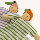 Two Nanchen baby comforters lying side by side: the Orange Baby Comforter in green and white stripes with an orange fruit hat, and the Peach Baby Comforter in lilac and white stripes with a pink fruit hat. Both dolls have soft, hand-embroidered faces and knotted feet.

