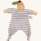 Front view of the Nanchen Peach Baby Comforter, a handmade doll with a soft, peach-colored face and pink velour fruit-shaped hat with a green leaf and brown stem. The doll has a lilac and white striped organic cotton terry body with knotted feet and outstretched arms, and a fabric label reading "Nanchen Natur" on the side.