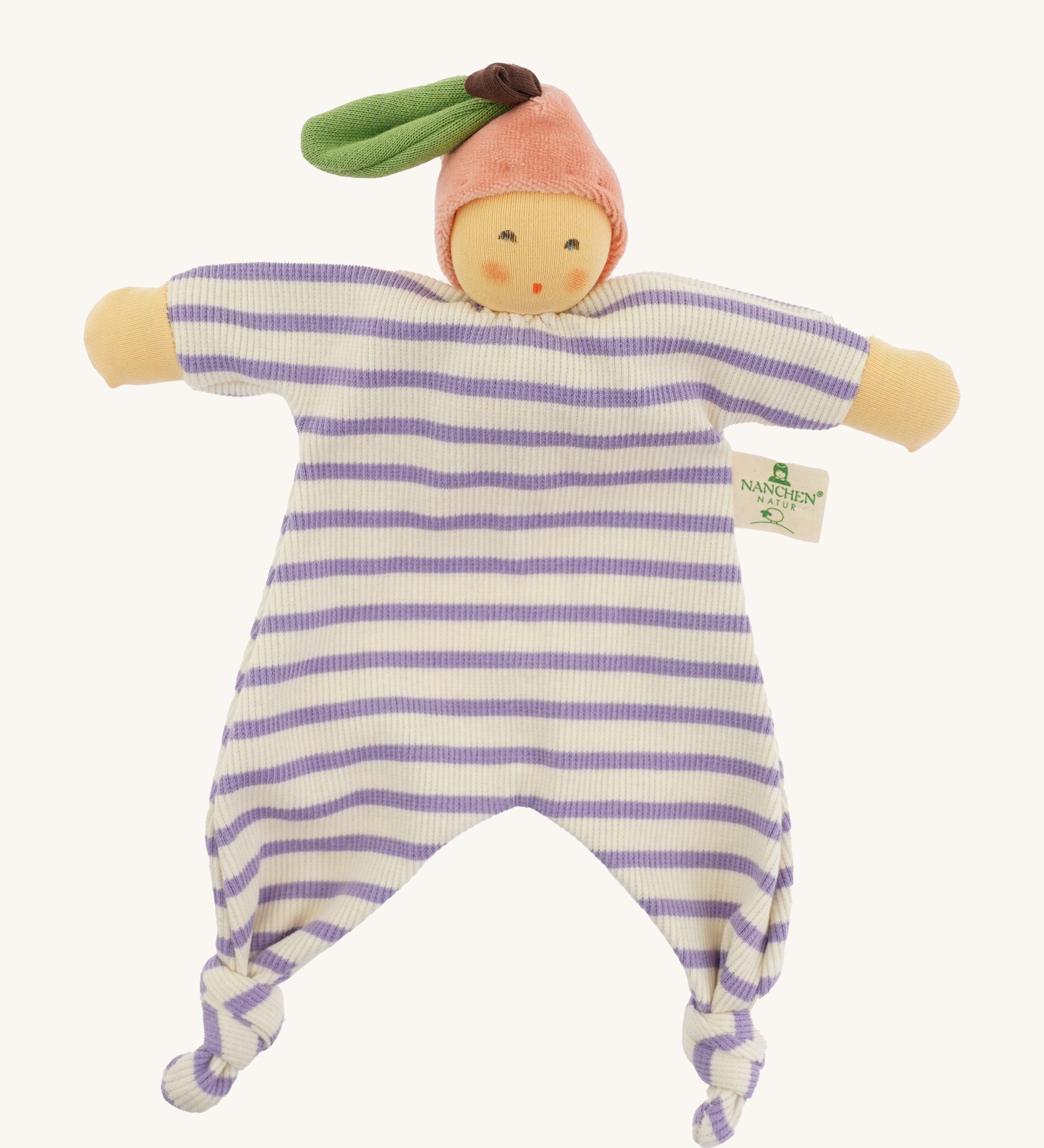 Front view of the Nanchen Peach Baby Comforter, a handmade doll with a soft, peach-colored face and pink velour fruit-shaped hat with a green leaf and brown stem. The doll has a lilac and white striped organic cotton terry body with knotted feet and outstretched arms, and a fabric label reading "Nanchen Natur" on the side.