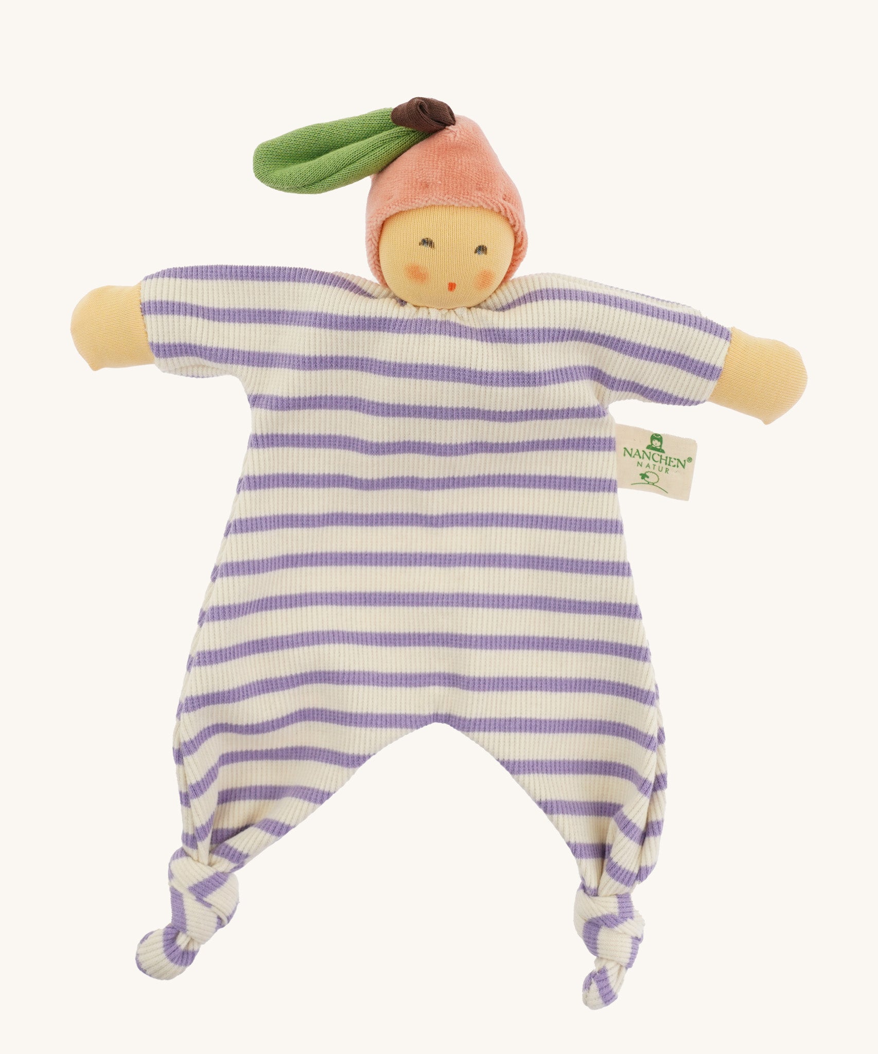 Front view of the Nanchen Peach Baby Comforter, a handmade doll with a soft, peach-colored face and pink velour fruit-shaped hat with a green leaf and brown stem. The doll has a lilac and white striped organic cotton terry body with knotted feet and outstretched arms, and a fabric label reading "Nanchen Natur" on the side.