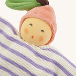 Close-up of the Nanchen Peach Baby Comforter, featuring a warm, peach-toned face with rosy cheeks and embroidered eyes and mouth. The doll wears a pink velour fruit-shaped hat with a green leaf and brown stem, and has a soft cotton body with lilac and white stripes.
