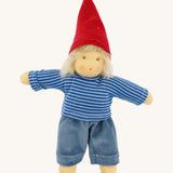 Front-facing image of the Nanchen Frederik handmade Waldorf doll fully dressed in its gnome-inspired outfit, wearing a red pointed hat, blue striped top, and blue trousers. The doll has soft blond mohair hair and a natural peach-toned cotton body.