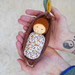 Nanchen Oak Baby Waldorf Doll - Floral. A little organic grasping doll in a brown velvet cradle in a persons hands.