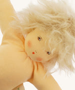 Close-up of a different Nanchen organic Waldorf doll with pale skin and fluffy platinum blond hair. The doll has a sweet hand-painted face with pink cheeks and red lips.