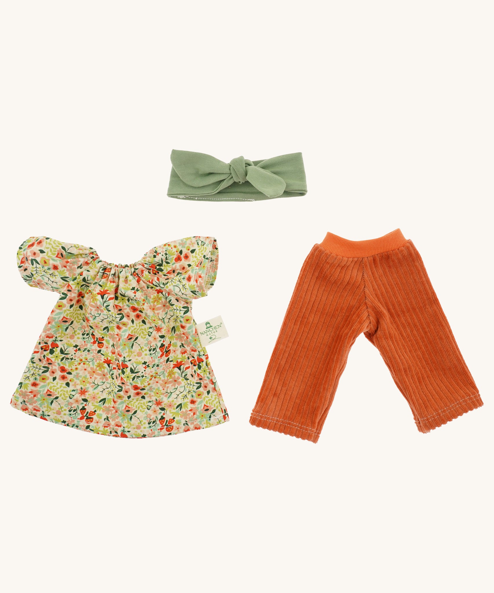 The Nanchen organic Waldorf doll Flore's removable outfit - a floral top, orange corduroy trousers, and a green hair bow.