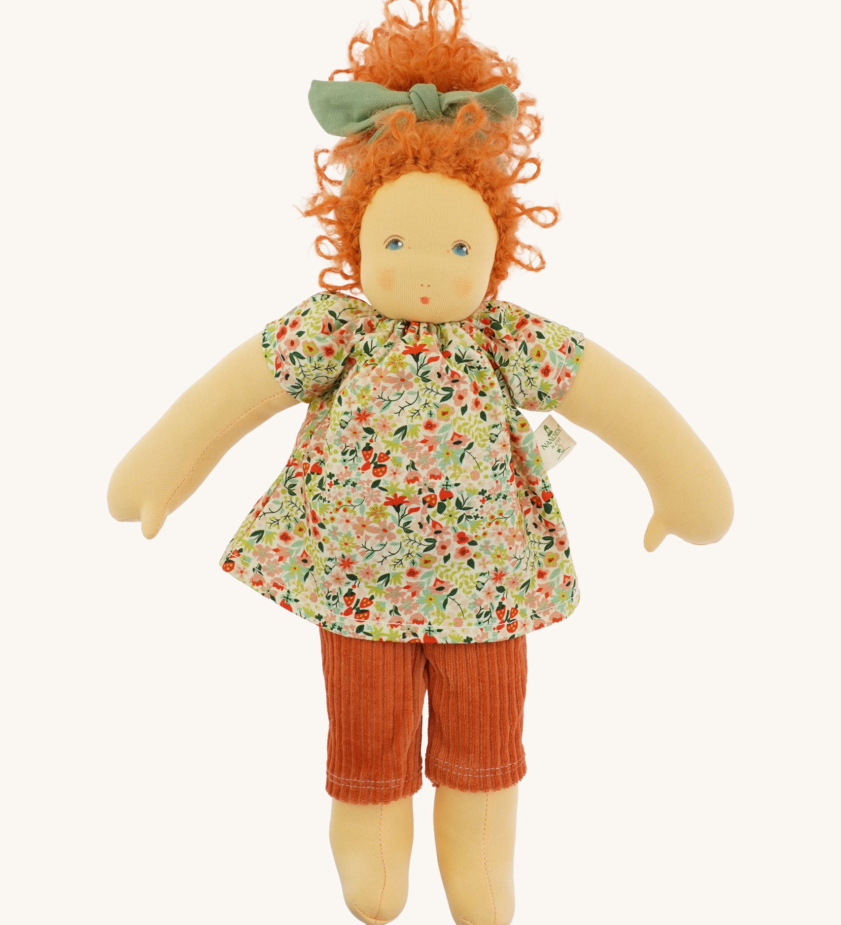 The Nanchen 'Flore' organic Waldorf doll, with curly red hair, a floral top, orange trousers, and a green hair bow.