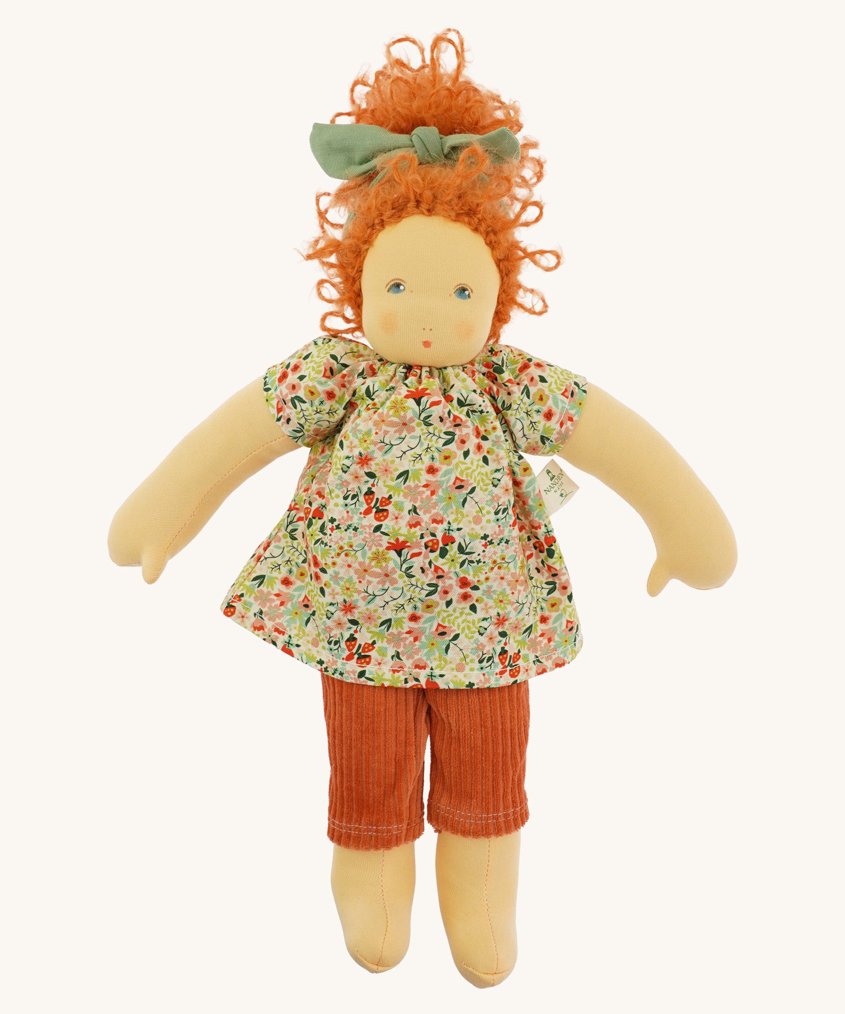 The Nanchen 'Flore' organic Waldorf doll, with curly red hair, a floral top, orange trousers, and a green hair bow.