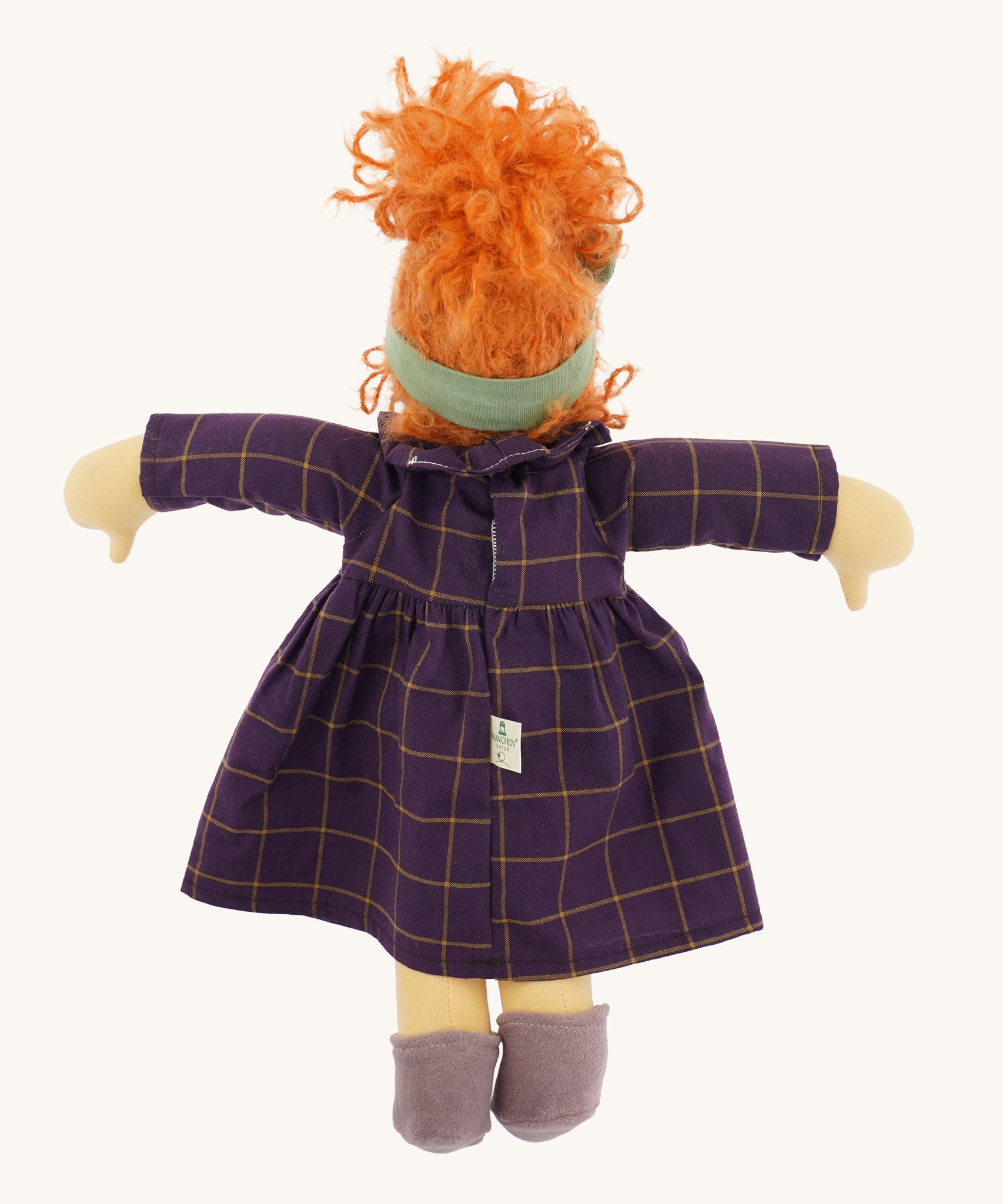 The back of the Nanchen 'Marlene' organic Waldorf doll, with curly red hair, a purple patterned dress, lilac shoes, and a green hair bow.