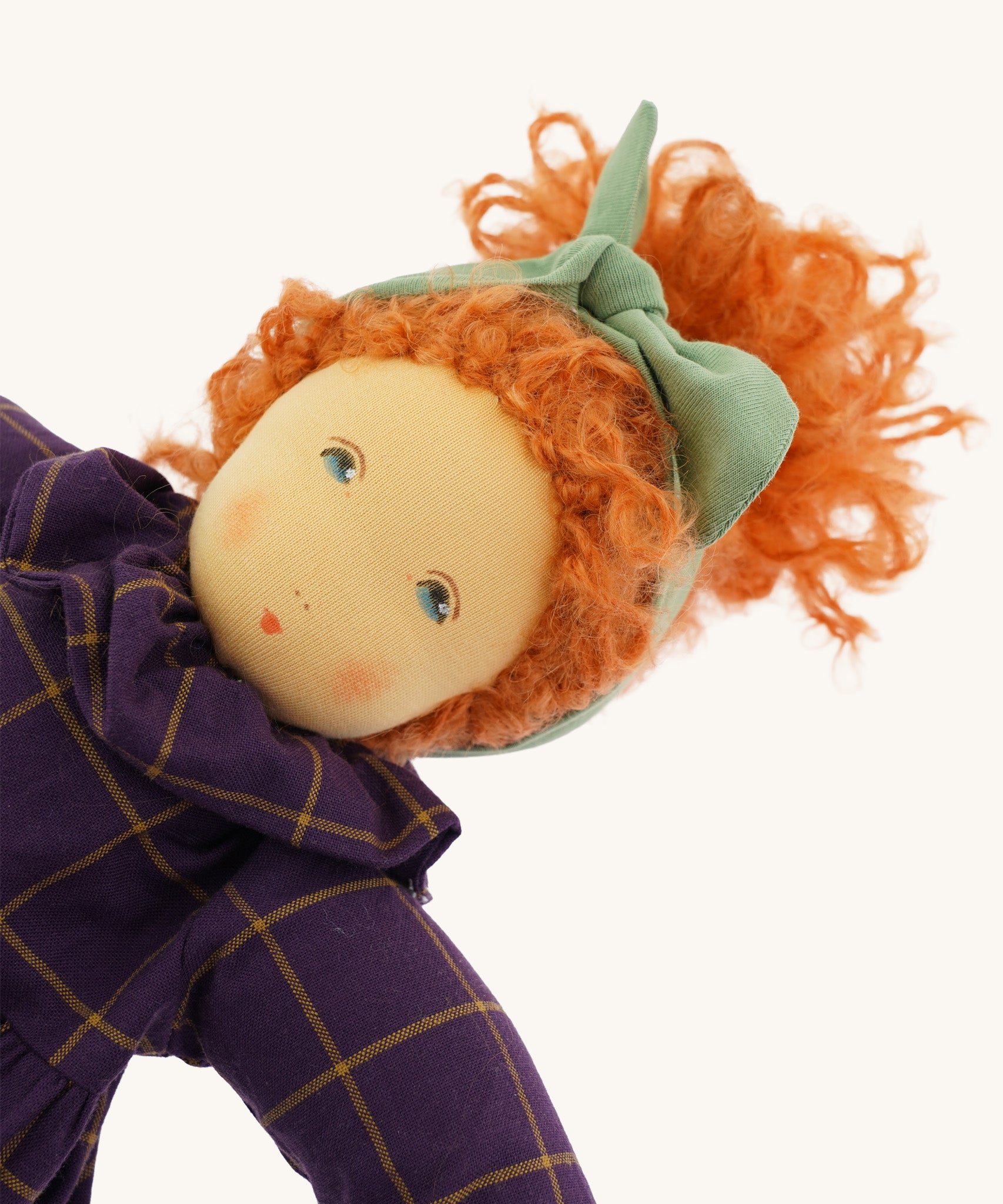 A closeup of the Nanchen 'Marlene' organic Waldorf doll, with curly red hair, a purple patterned dress, and blue eyes
