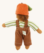 Back view of the same Nanchen organic Waldorf doll wearing the full outfit including the orange fruit hat with green leaf, showing the doll's wild brown hair and sewn-in brand tag.