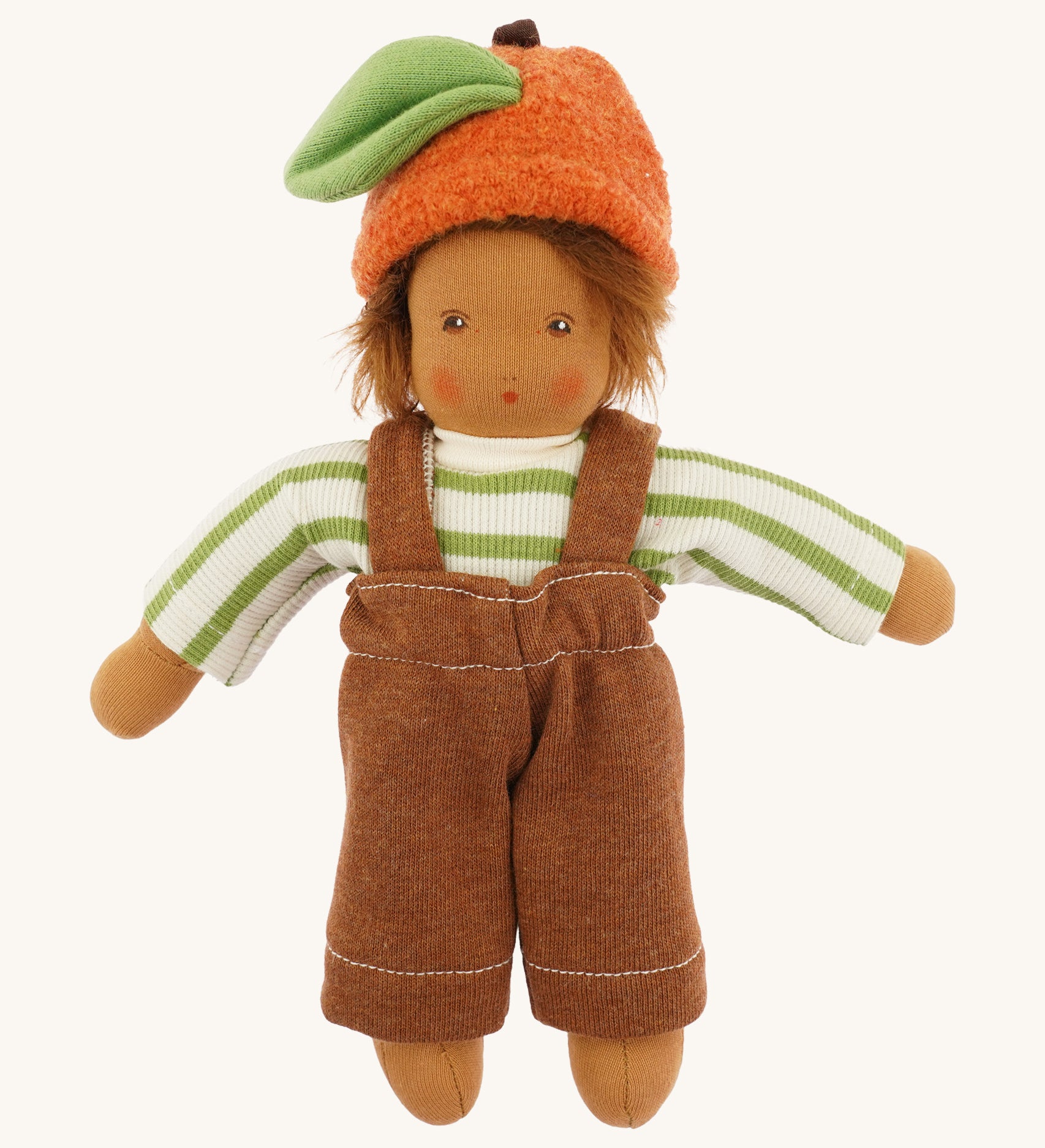 Front view of the dressed Nanchen organic Waldorf doll in green striped top, brown dungarees, and orange fruit hat with green leaf. The doll has brown skin and spiky brown hair.