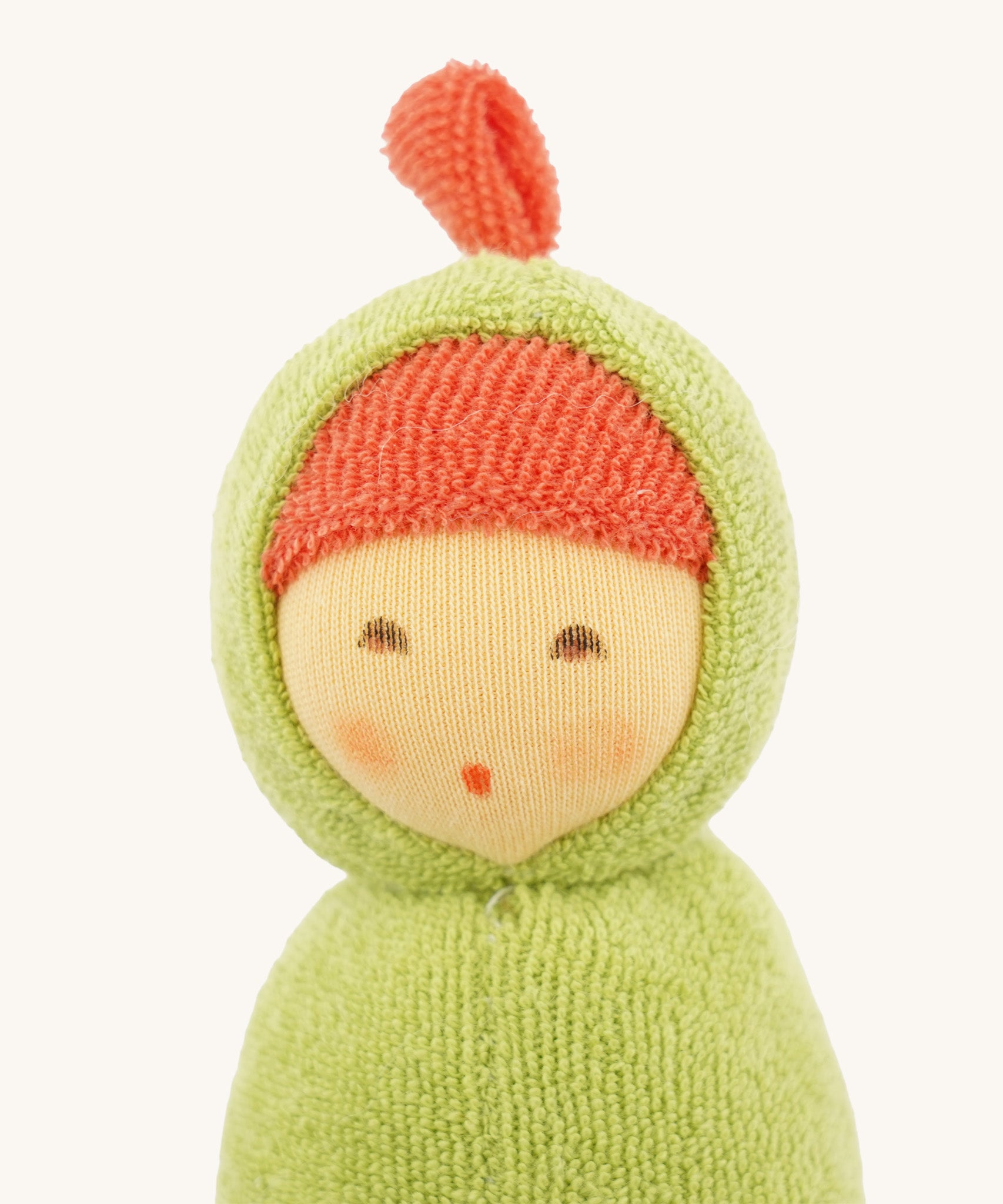 Close-up of the Nanchen Pea Pod Rattle Doll’s face, showing its delicately hand-painted features including closed eyes and a small mouth. The doll wears a red terry bonnet under a green hood with a small top knot.

