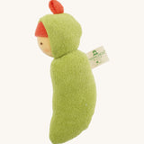 Side view of the Nanchen Pea Pod Rattle Doll, highlighting the curved shape of its green terry cotton body and the attached Nanchen Natur tag. The red fabric top knot is visible on the hood.
