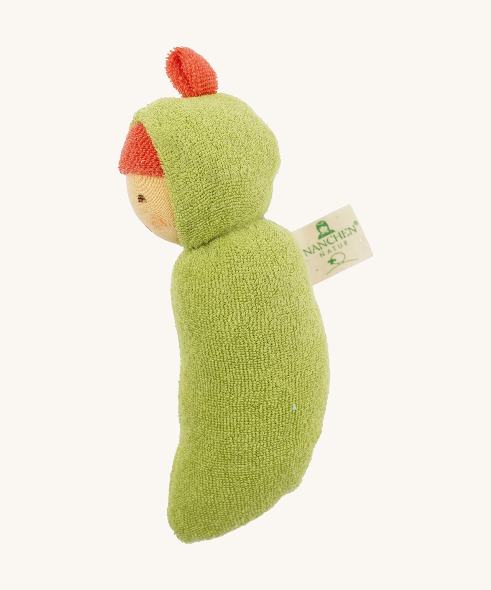 Side view of the Nanchen Pea Pod Rattle Doll, highlighting the curved shape of its green terry cotton body and the attached Nanchen Natur tag. The red fabric top knot is visible on the hood.
