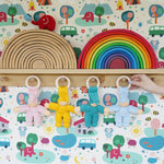 Four Pimpel doll comforters hung up by their wooden hops on wooden pegs on a shelf. There are pink, yellow, turquoise and light blue dolls. 