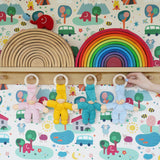 Four Pimpel doll comforters hung up by their wooden hops on wooden pegs on a shelf. There are pink, yellow, turquoise and light blue dolls. 