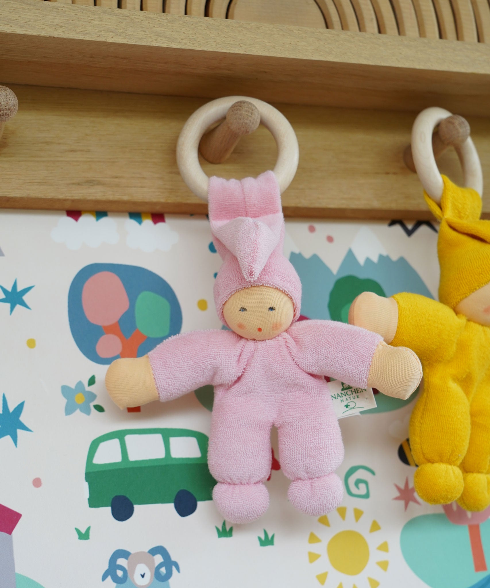 A Pink Nanchen Pimpel Waldorf Doll Ring Comforter hung up by it's wooden ring on a wooden peg on a shelf.