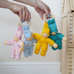 Four Pimpel doll baby comfortmers being held up in an adult's hands. There is a pink, light blue, yellow and turquoise doll. 