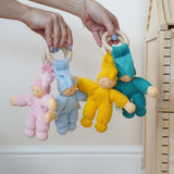 Four Pimpel doll baby comfortmers being held up in an adult's hands. There is a pink, light blue, yellow and turquoise doll. 