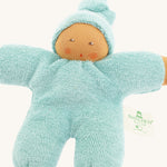 Close-up of the Nanchen Pimpel Waldorf Doll in sage green, showing its soft terry cotton body and sweet hand-painted facial features. The doll wears a pointed hood and has rosy cheeks, with a "Nanchen Natur" tag on its side.