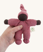 A Nanchen Pimpel Waldorf Handcrafted Doll with a berry pink coloured outfit an matching knotted hat in an adult's hand.