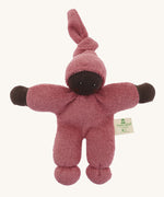 A Nanchen Pimpel Waldorf Handcrafted Doll with a berry pink coloured outfit an matching knotted hat. The doll has dark brown coloured skin. 