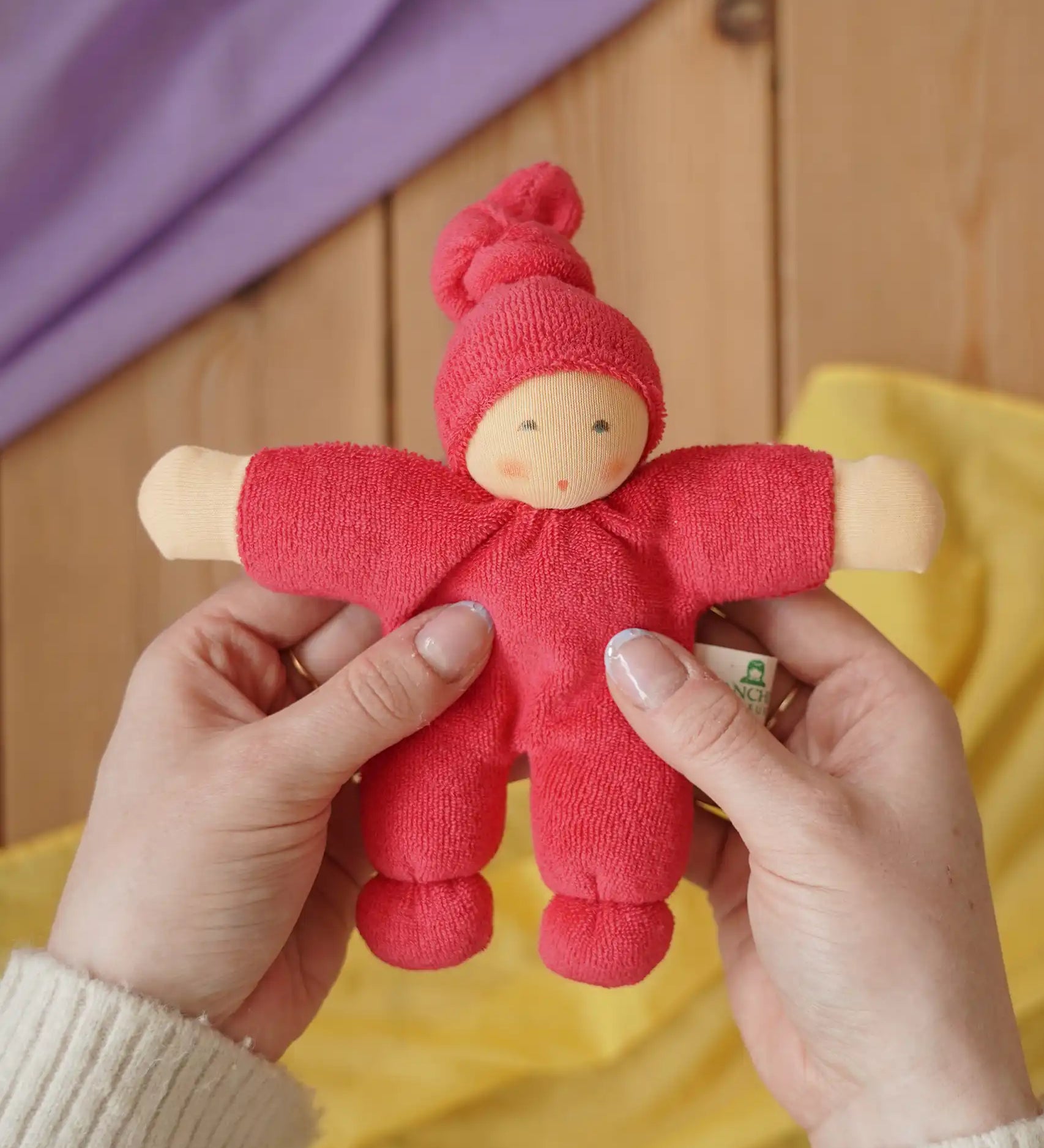Nanchen Natur Pimpel Waldorf doll in cherry red in an adult's hands in the Babipur playroom. 