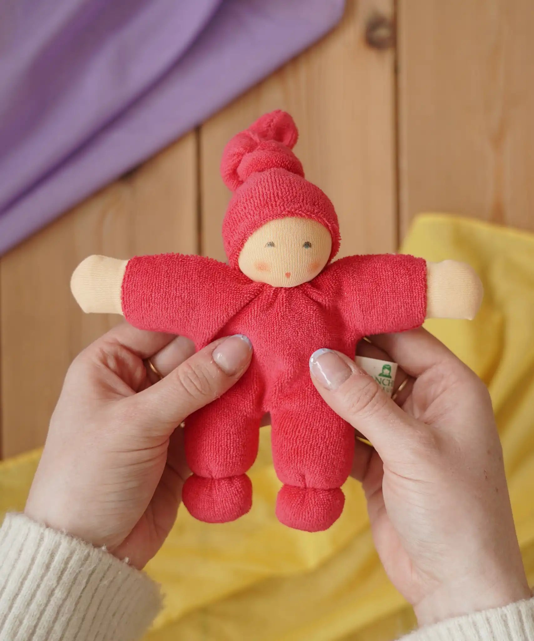 Nanchen Natur Pimpel Waldorf doll in cherry red in an adult's hands in the Babipur playroom. 