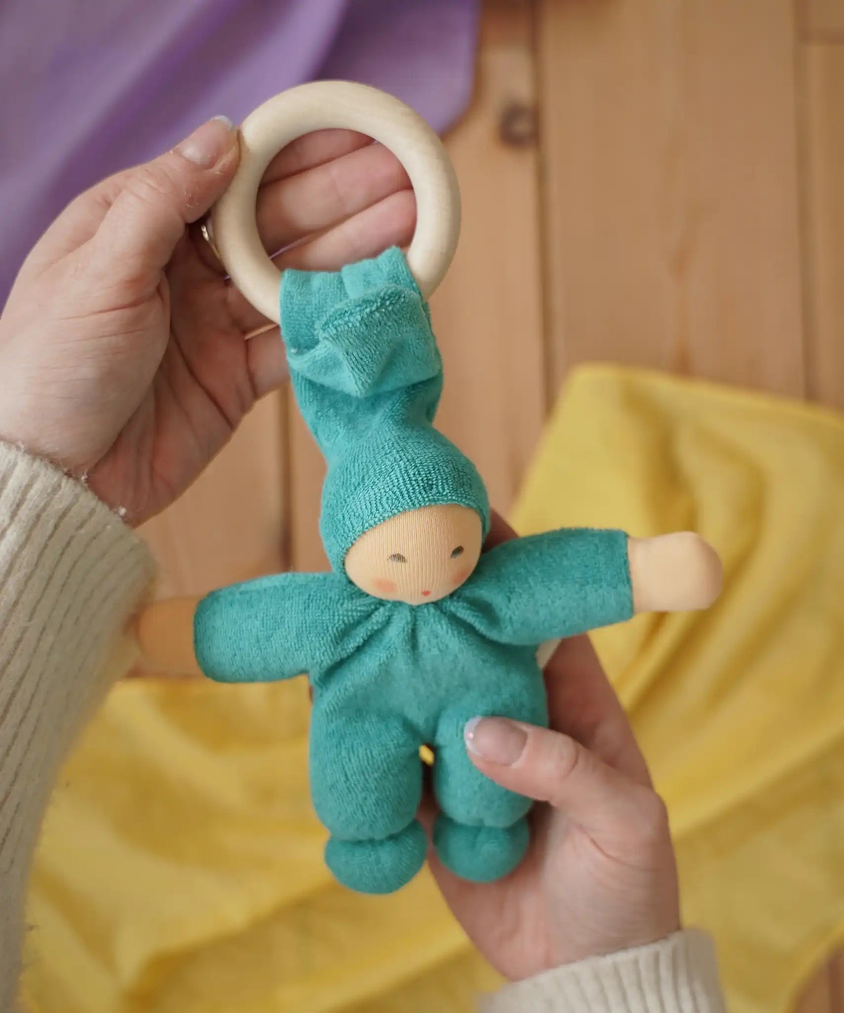 A turquoise coloured Nanchen Pimpel Waldorf Doll Ring Comforter in an adult's hands in the Babipur playroom. 