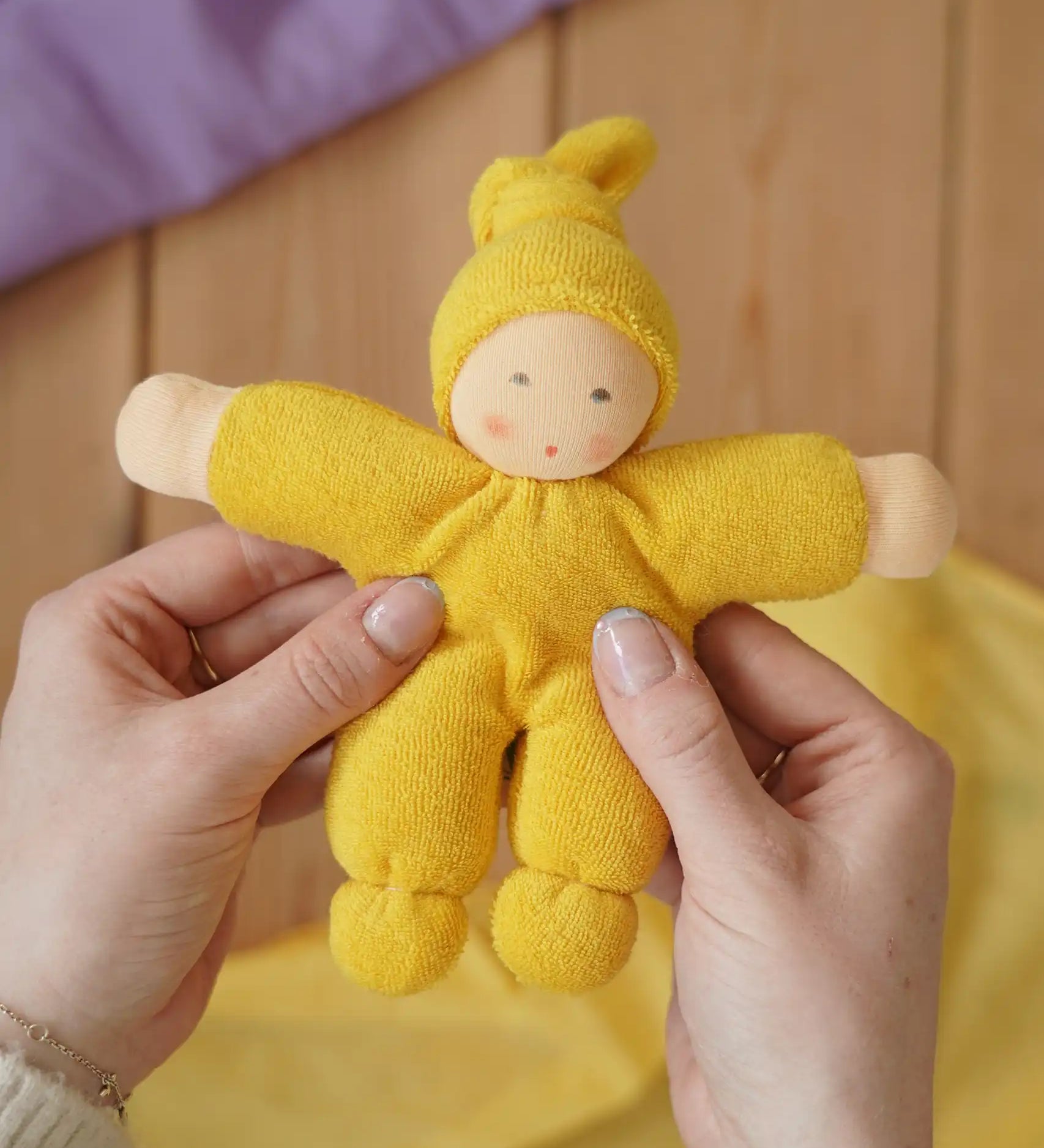 Nanchen Natur Pimpel Waldorf doll in yellow in an adult's hands in the Babipur playroom. 