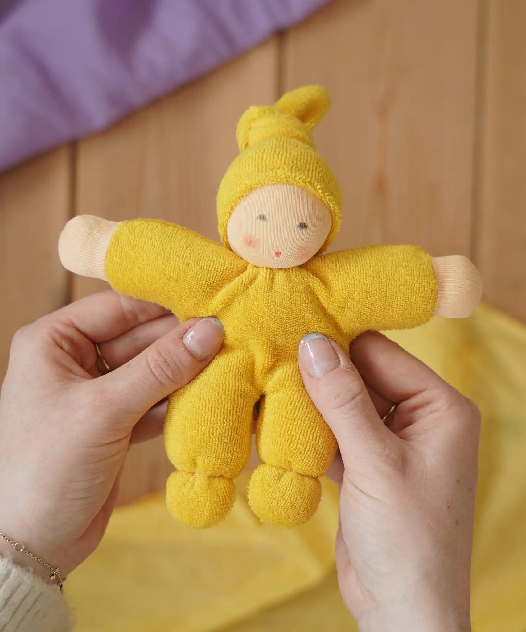 Nanchen Natur Pimpel Waldorf doll in yellow in an adult's hands in the Babipur playroom. 