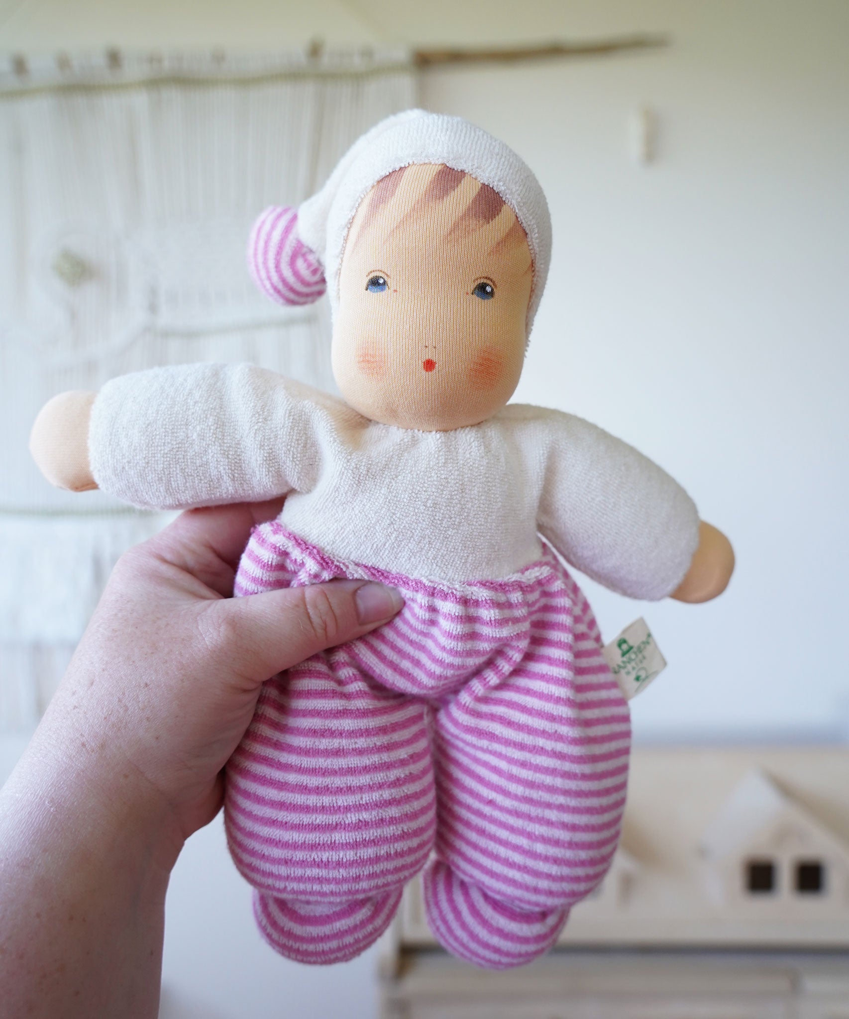 A Nanchen Möpschen Waldorf Doll with Pink Striped outfit in an adult's hand.