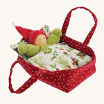 A Nanchen red with white dots carry cot for a Nanchen doll tucked in a garden blanket on a cream background.