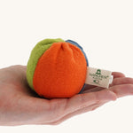 Nanchen small Colourful, Organic Baby Rattle Ball on a hand for scale. This is a soft terry material in blue, orange and green colours on a cream background.