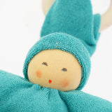 Close-up of the Nanchen Pimpel Doll in vibrant turquoise. The doll's painted facial features include soft blush cheeks and a red mouth, peeking out from under a cozy turquoise hood made of organic cotton terry. A wooden teething ring is looped through the pointed hat.
