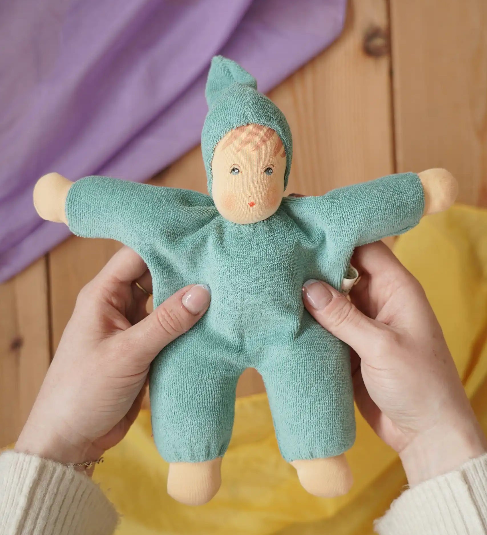 Nanchen Natur Waldorf cuddle doll in turquoise in an adult's hands in the Babipur playroom. 
