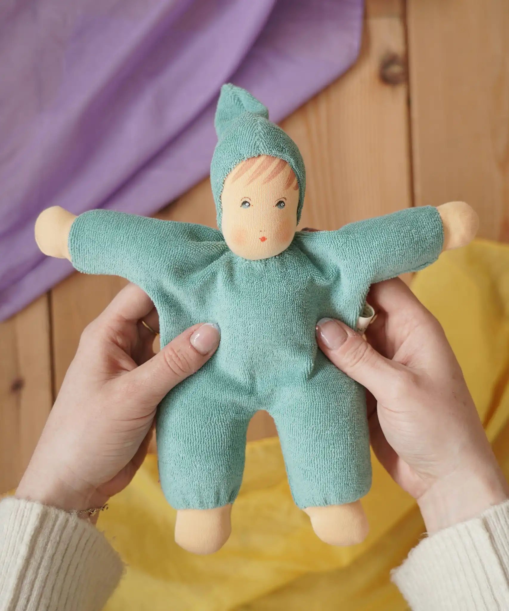 Nanchen Natur Waldorf cuddle doll in turquoise in an adult's hands in the Babipur playroom. 