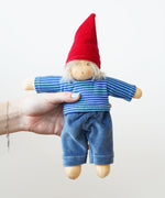 A Nanchen Frederik Waldorf Doll being held in an adult's hand. The doll has white blonde hair and is wearing a gnome inspired outfit.