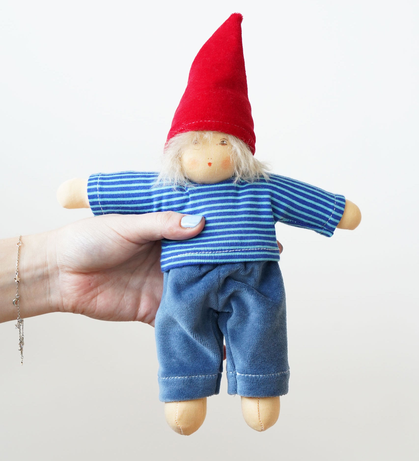 A Nanchen Frederik Waldorf Doll being held in an adult's hand. The doll has white blonde hair and is wearing a gnome inspired outfit.