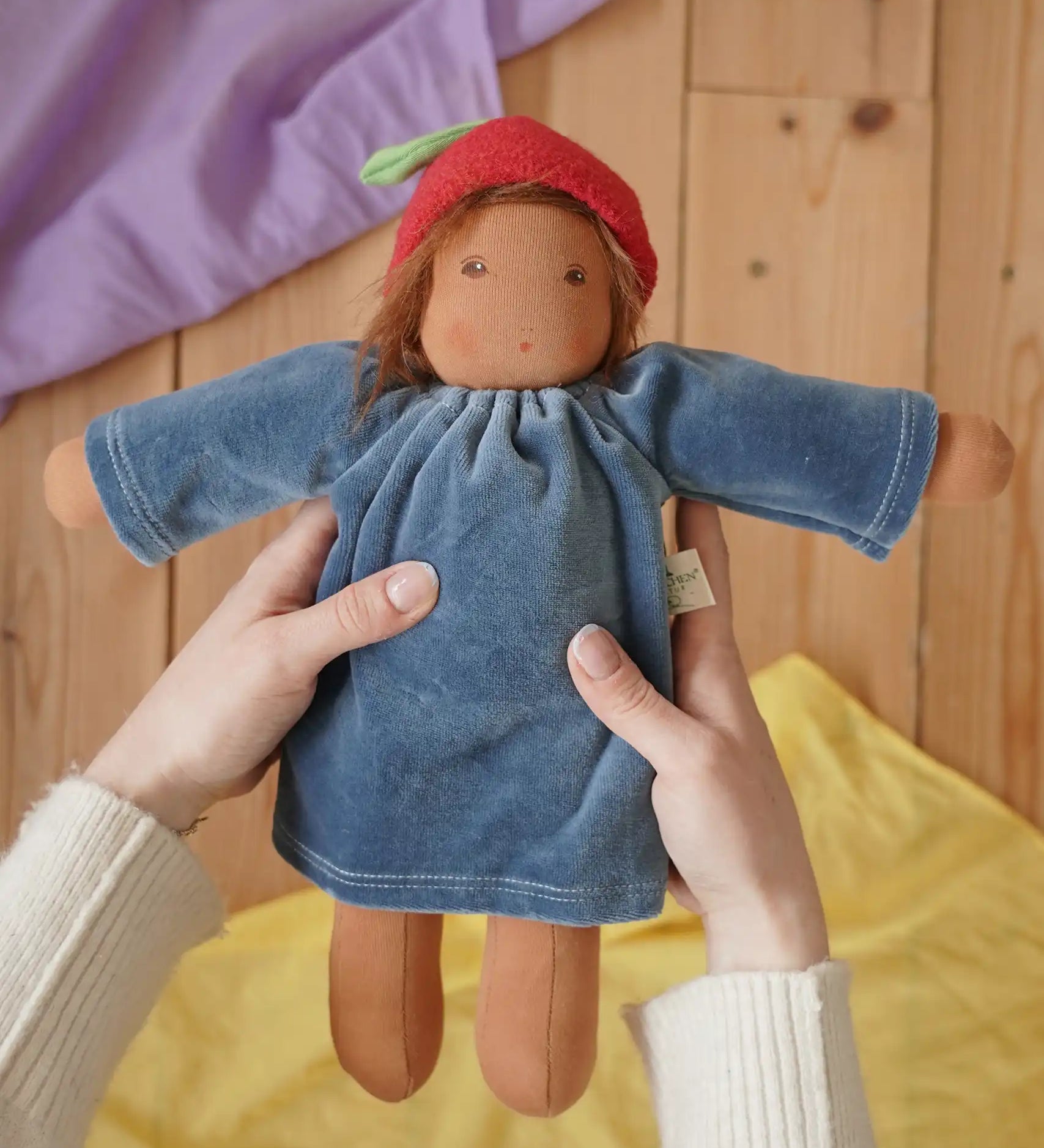 Nanchen Waldorf Doll Garden Child lene with apple hat in an adult's hand in the Babipur playroom. 