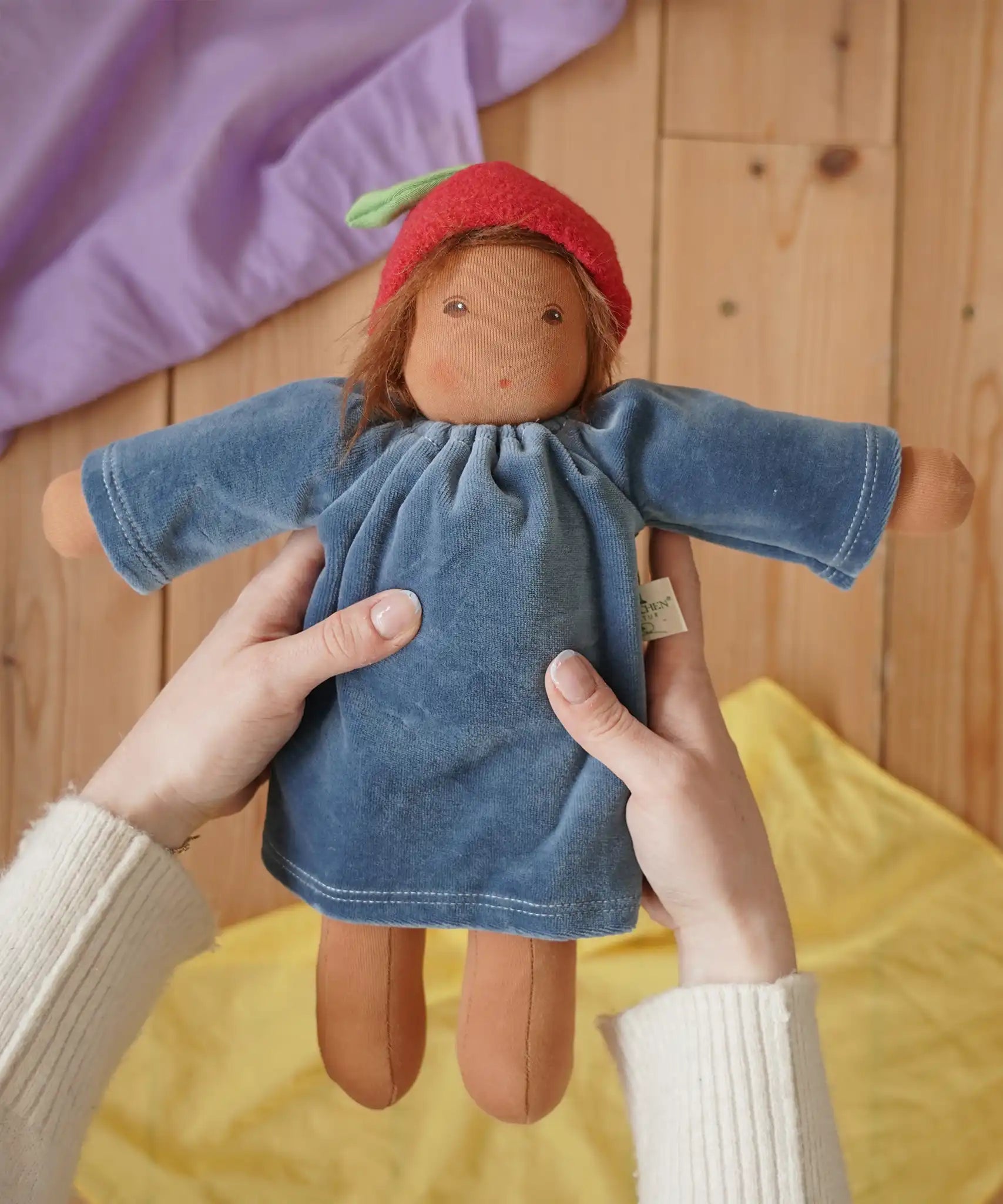 Nanchen Waldorf Doll Garden Child lene with apple hat in an adult's hand in the Babipur playroom. 