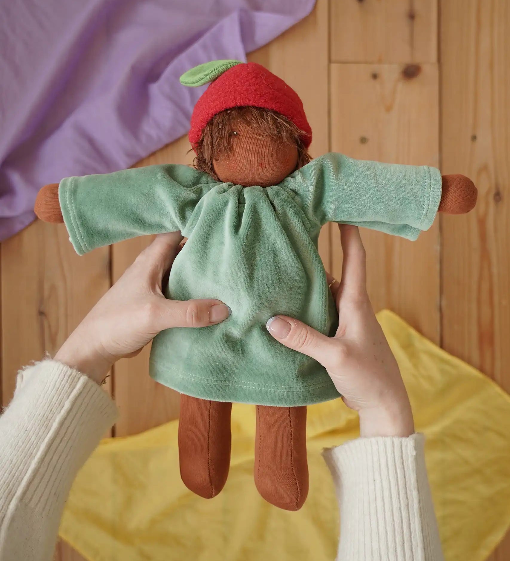 Nanchen Waldorf doll garden child Lilly with apple hat in an adult's hand in the Babipur playroom.