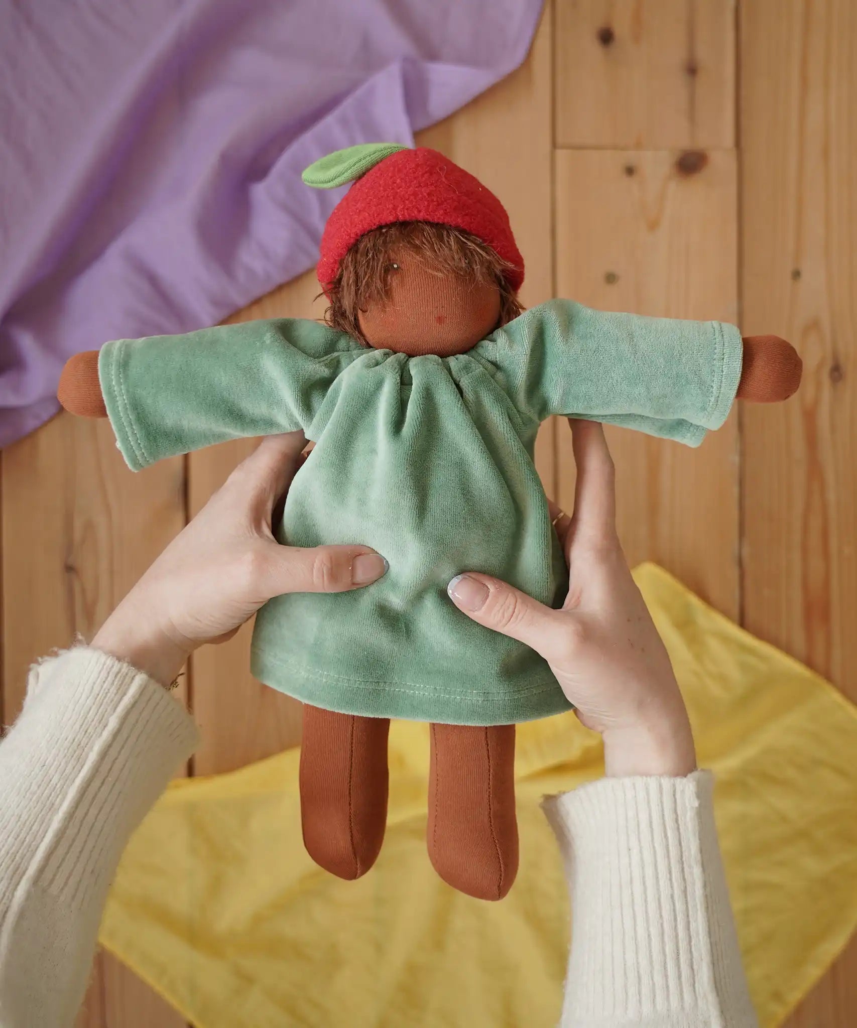 Nanchen Waldorf doll garden child Lilly with apple hat in an adult's hand in the Babipur playroom.