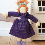 A Nanchen Marlene Waldorf Doll being held up in an adult's hand. A Plan Toys Victorian dolls house can be just off to the right side.