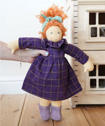 A Nanchen Marlene Waldorf Doll being held up in an adult's hand. A Plan Toys Victorian dolls house can be just off to the right side.