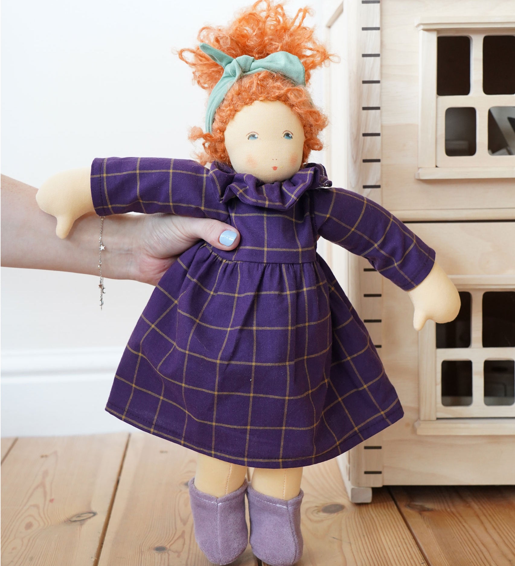 A Nanchen Marlene Waldorf Doll being held up in an adult's hand. A Plan Toys Victorian dolls house can be just off to the right side.