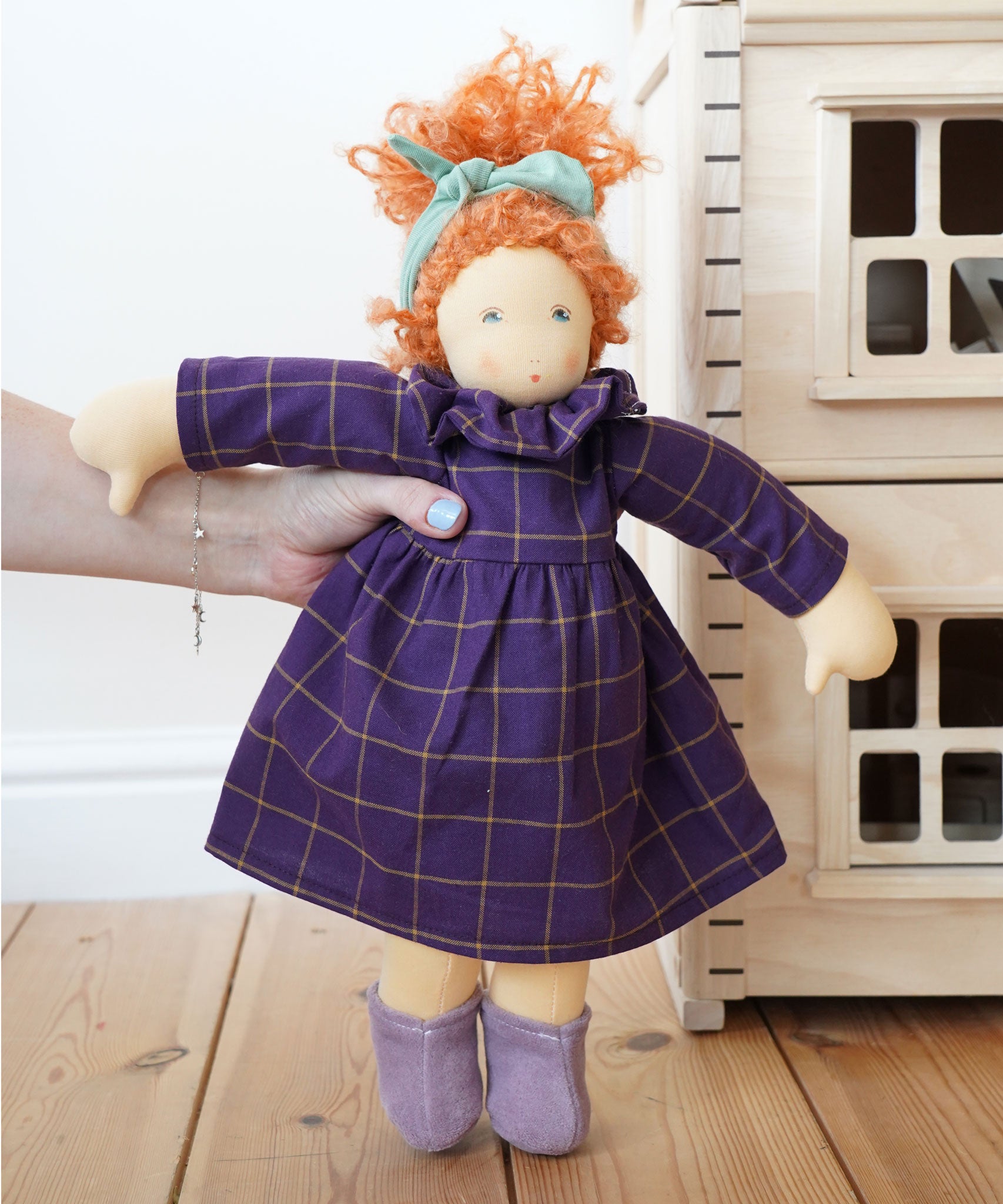 A Nanchen Marlene Waldorf Doll being held up in an adult's hand. A Plan Toys Victorian dolls house can be just off to the right side.