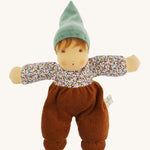 Nanchen Forest Child Waldorf Doll - Sage. This beautifully handcrafted doll wears sage velour trousers, a brown hat and a floral top. On a cream background