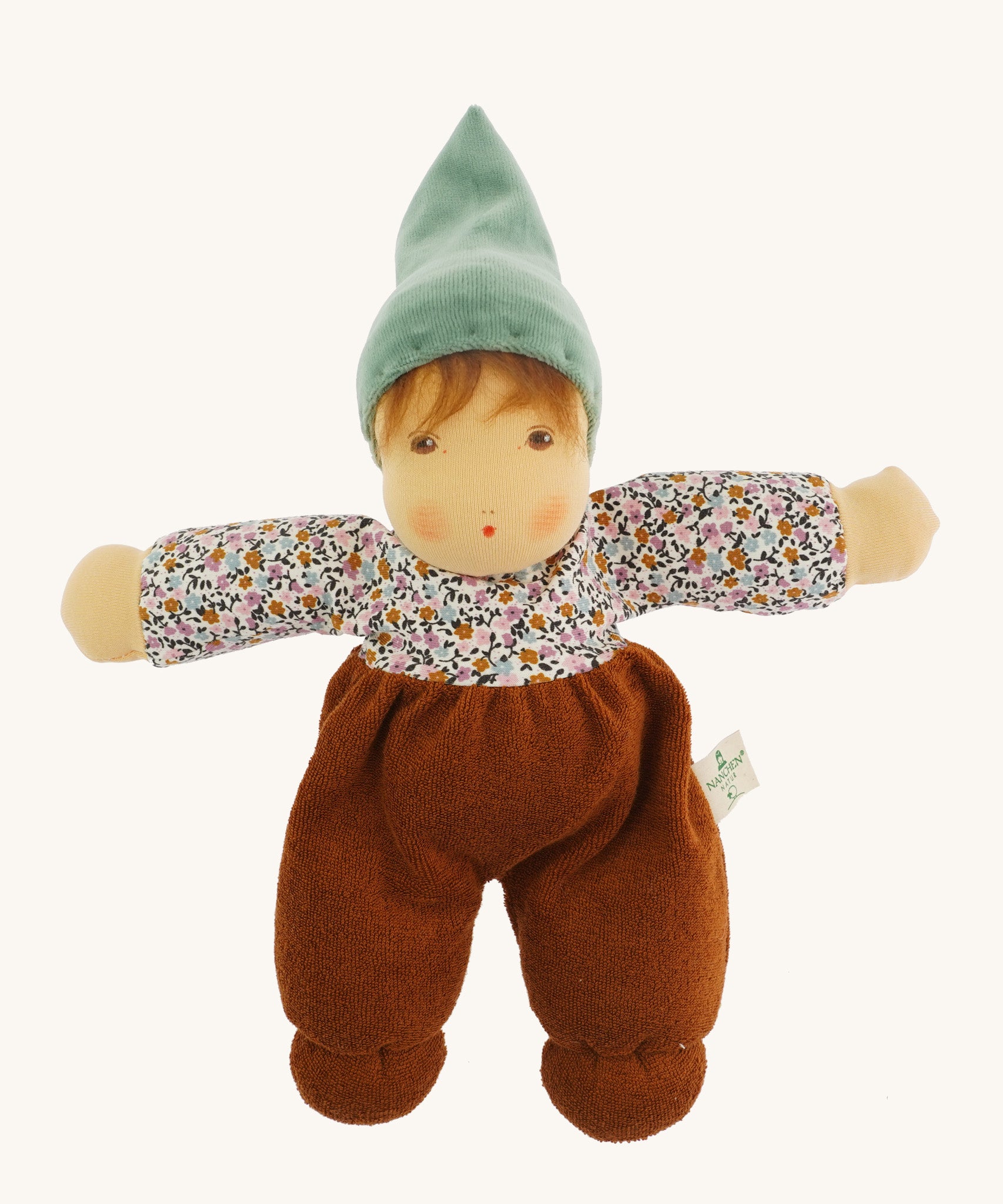 Nanchen Forest Child Waldorf Doll - Sage. This beautifully handcrafted doll wears sage velour trousers, a brown hat and a floral top. On a cream background